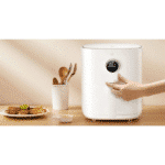 A person interacting with the White Xiaomi Smart Air Fryer in a kitchen setting, next to a plate of cooked food and utensils